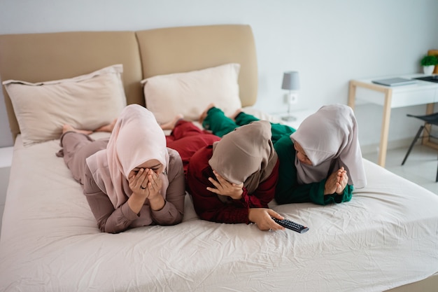 Tres mujeres con velo acostado en la cama y asustan mientras ven la televisión