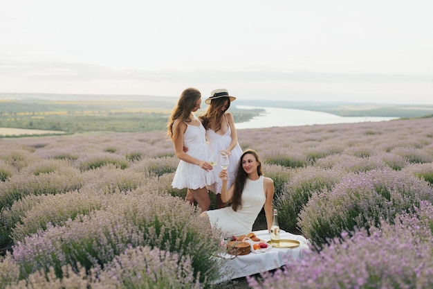 Tres mujeres vestidas de blanco se sientan en un campo de lavanda.