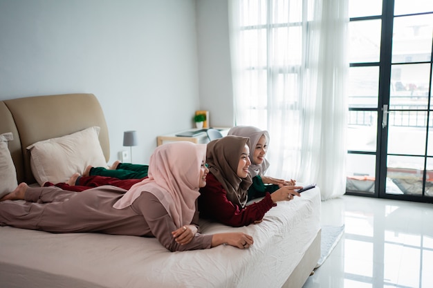 Três mulher com véu deitado na cama gostam de assistir tv