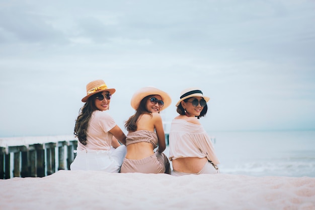 Três mulher usando chapéu de palha sentado na praia do mar de férias