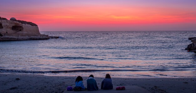 Três mulheres esperando o nascer do sol em frente ao mar (região de puglia, sul da itália). conceito de amizade, viagens e aventura.