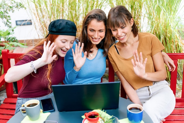 Três mulheres jovens e felizes e sorridentes fazendo uma videochamada em um laptop acenando em saudação para a tela para comunicação de longa distância