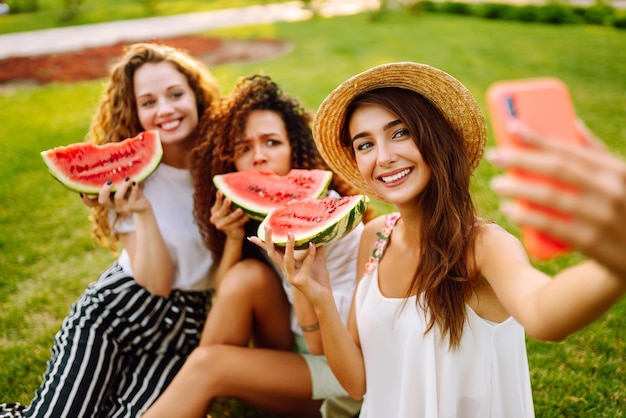 Três mulheres jovens se divertem juntas e comem melancia em um dia quente de verão
