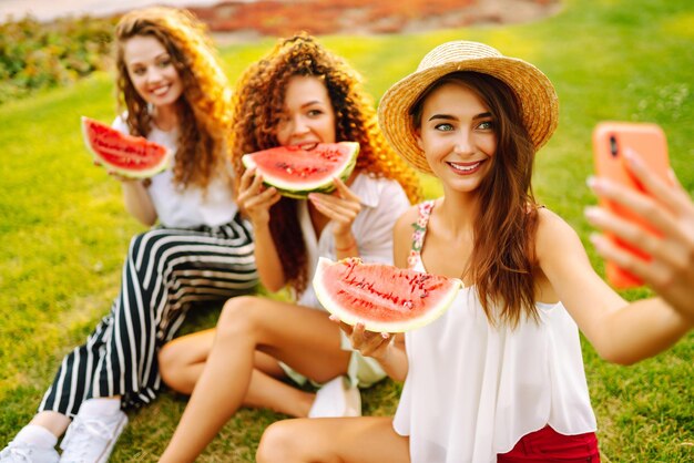 Três mulheres jovens se divertem juntas e comem melancia em um dia quente de verão