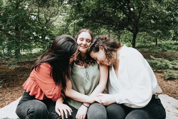 Foto três mulheres se abraçando enquanto sorriem para a câmera em uma floresta, multicultural, jovem, amor, carinho e conceito de amizade