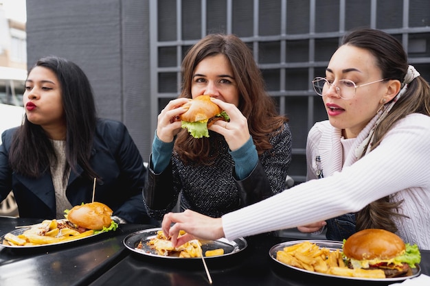 Três mulheres sentadas no restaurante de mesa comendo batatas fritas e cheeseburguer.