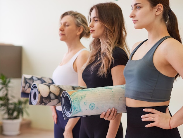 Três mulheres vestindo roupas ativas seguram tapetes de ioga prontos para começar a treinar o conceito de esportes