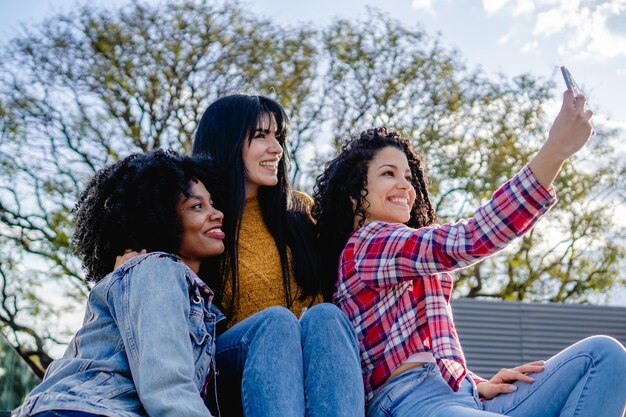 Três namoradas multirraciais tirando uma selfie em um parque da cidade