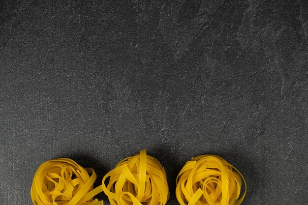 Tres nidos de fettuccine caseros aislados sobre fondo oscuro