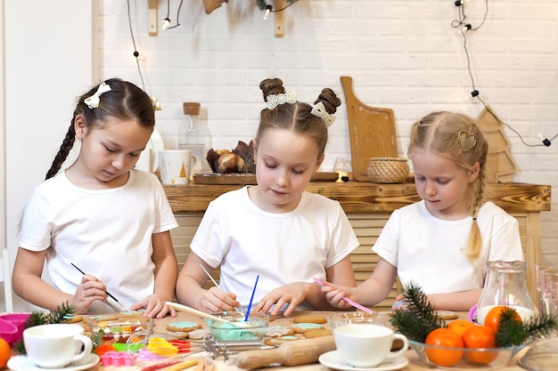 Tres niñas en la cocina decoran el pan de jengibre horneado terminado con glaseado dulce y crema cocinando vacaciones familiares