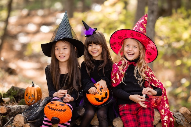 Tres niñas en disfraces de brujas de halloween ríen evocan caminar por el bosque de otoño