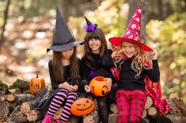 Tres niñas con disfraces de brujas reír evocar caminar por el bosque otoñal con cestas