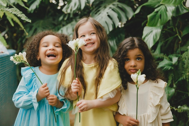 Tres niñas en el jardín con flores en las manos niños de diferentes nacionalidades