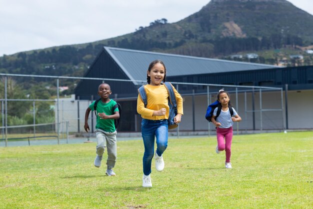 Tres niños corren alegremente por un campo cubierto de hierba durante el día en la escuela