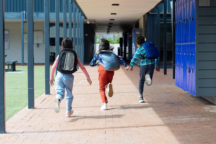 Foto tres niños corren por un pasillo de la escuela con mochilas a remolque