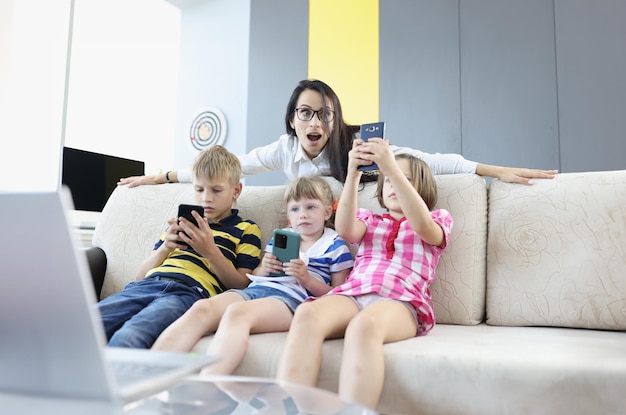 Foto tres niños están sentados en el sofá con teléfonos inteligentes en las manos jugando juegos en línea con una mujer