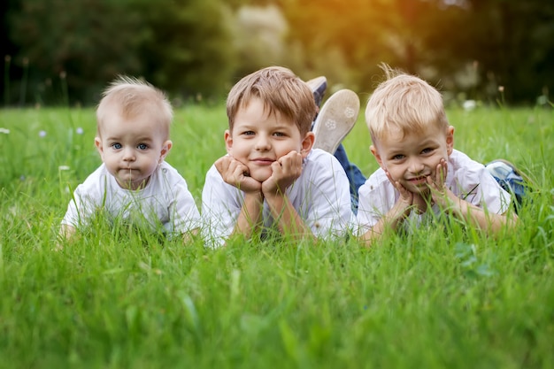 Tres niños felices (hermanos) descansando sobre la hierba verde en verano