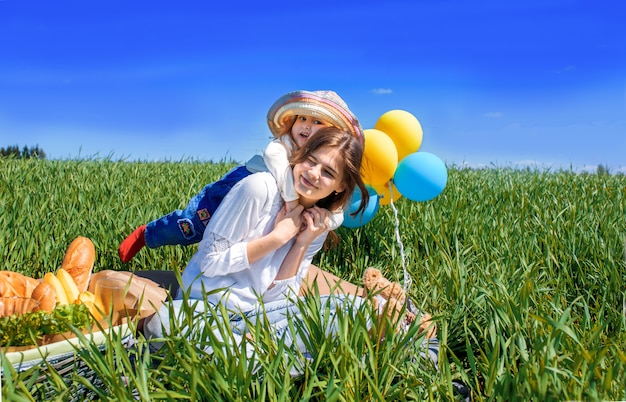 Tres niños felices sentados en picnic en el campo. cielo azul, hierba verde. pan, pasteles y frutas en una canasta.