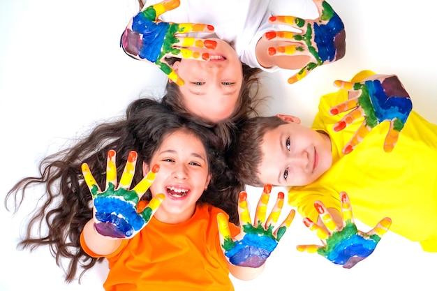 Tres niños felices y sonrientes están mirando a la cámara y extendiendo sus manos en pinturas.