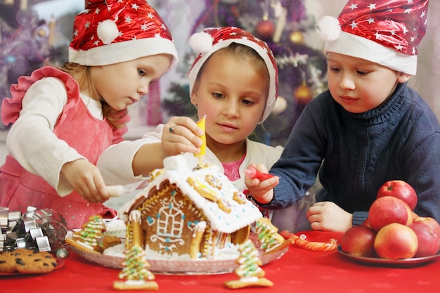 Tres niños con gorras decoradas casa de jengibre.