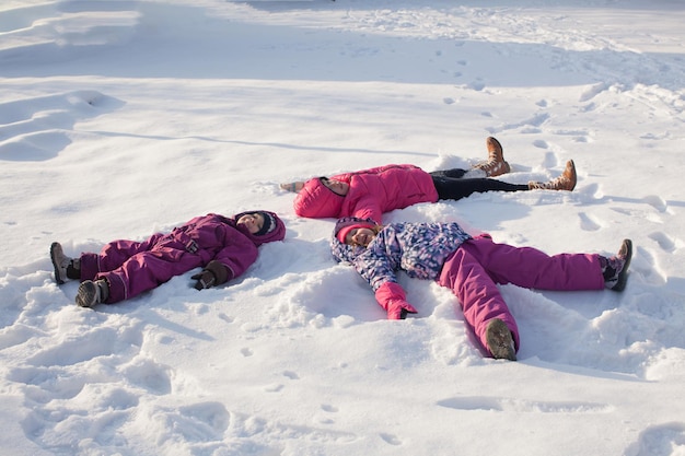 Tres niños hacen ángeles de nieve en un día soleado de invierno
