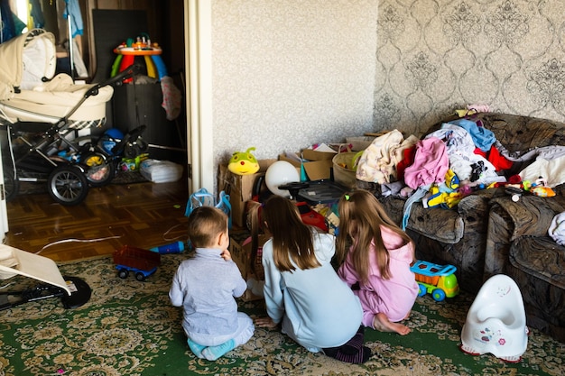 Tres niños irreconocibles están jugando en una habitación sucia y desordenada