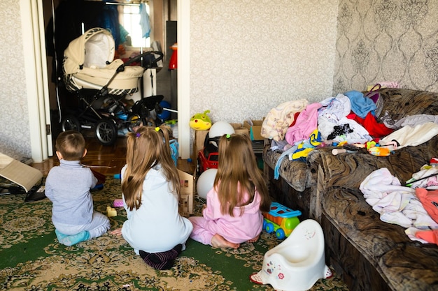 Tres niños irreconocibles están jugando en una habitación sucia y desordenada