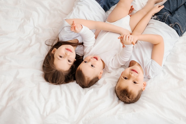 Tres niños pequeños yacen en la cama y abrazan, vista desde arriba. hermanos, familia numerosa