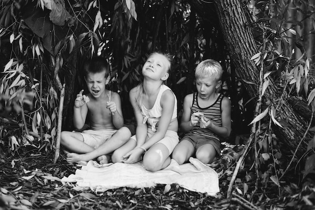 Tres niños del pueblo juegan en una choza que ellos mismos han construido con hojas y ramitas Casa de madera en el bosque Fotografía en blanco y negro