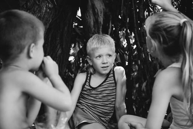 Tres niños del pueblo juegan en una choza que ellos mismos han construido con hojas y ramitas Casa de madera en el bosque Fotografía en blanco y negro