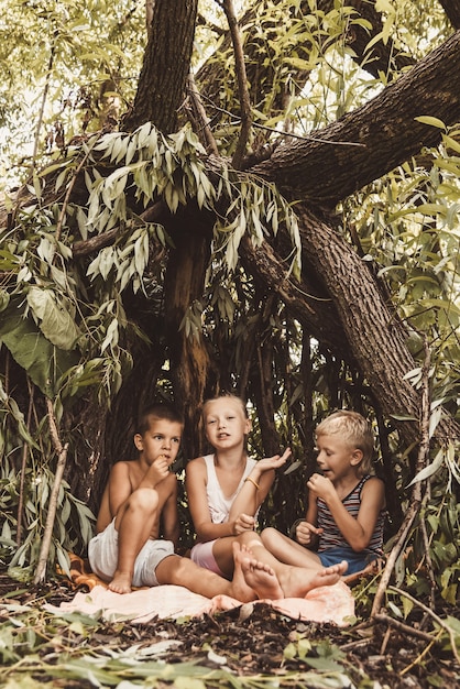 Tres niños del pueblo juegan en una choza que ellos mismos han construido con hojas y ramitas.