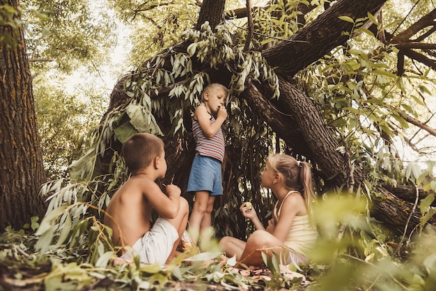 Foto tres niños del pueblo juegan en una choza que ellos mismos han construido con hojas y ramitas.