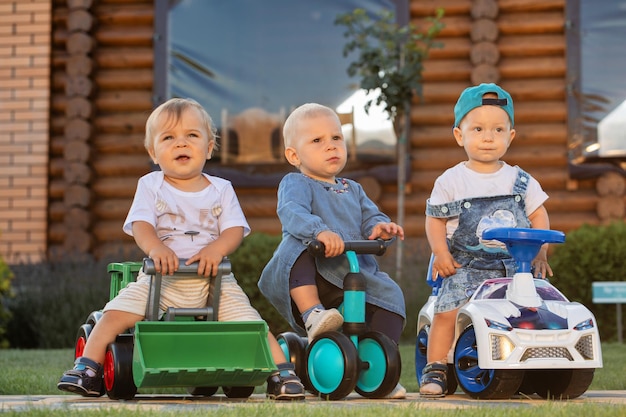 Tres niños viajan en vehículos de juguete en el patio trasero.