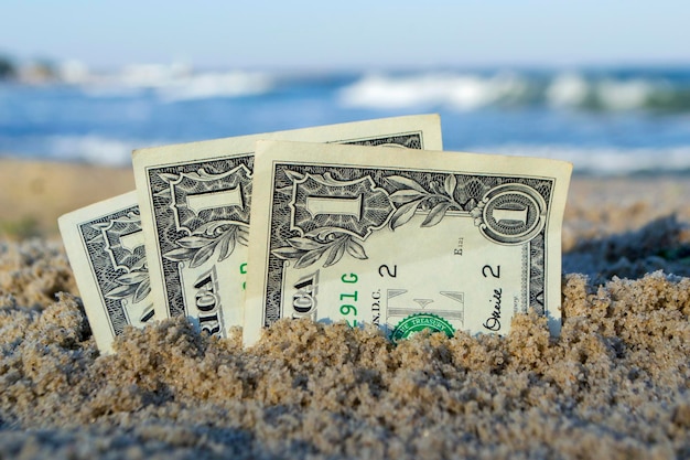 Três notas de um dólar cavadas a meio caminho na areia na praia do mar em dia ensolarado