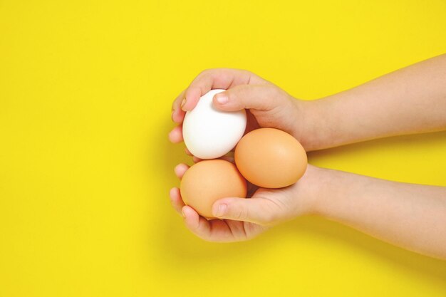 Três ovos de galinha nas mãos de um menino em um fundo amarelo.