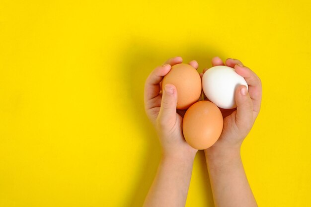 Três ovos de galinha nas mãos de um menino em um fundo amarelo.