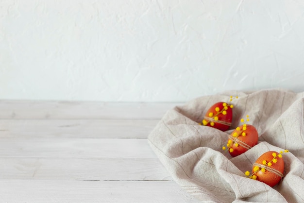 Três ovos de páscoa marrons decorados com flores de mimosa em têxteis de algodão em fundo branco de madeira, copie o espaço