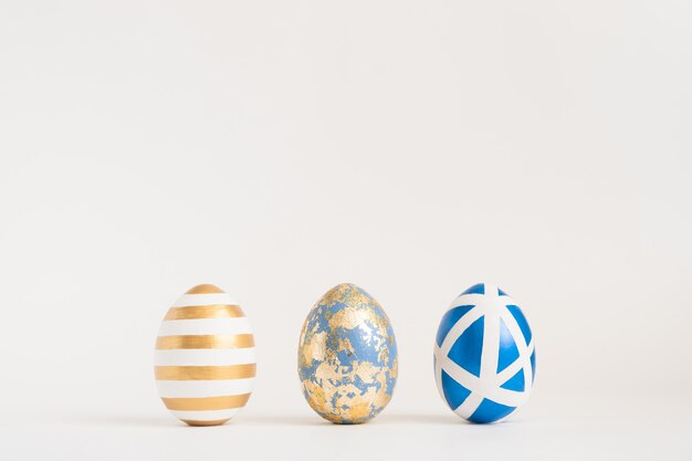 Três ovos decorados dourados da Páscoa na superfície azul. Conceito mínimo de Páscoa.