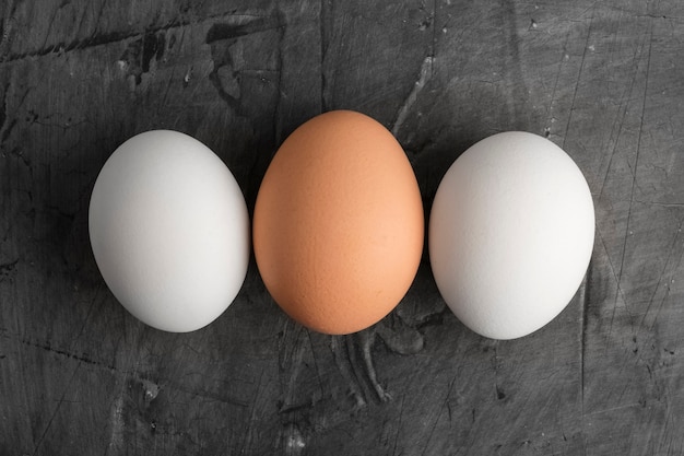 Três ovos, dois brancos e um marrom em um fundo preto. Copie o espaço