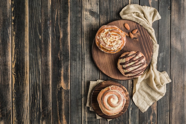 Três pães de Cinnabon em uma placa de madeira com um guardanapo em um fundo escuro. Pão clássico americano.