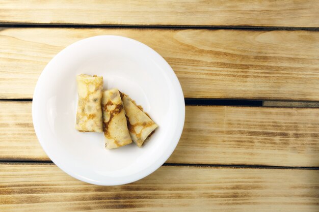 Tres panqueques, en un plato blanco sobre una pared de madera con espacio de copia.