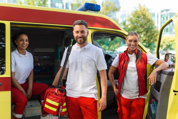 Três paramédicos pela ambulância Jovem e homem sorrindo O médico está carregando uma bolsa de trauma médico