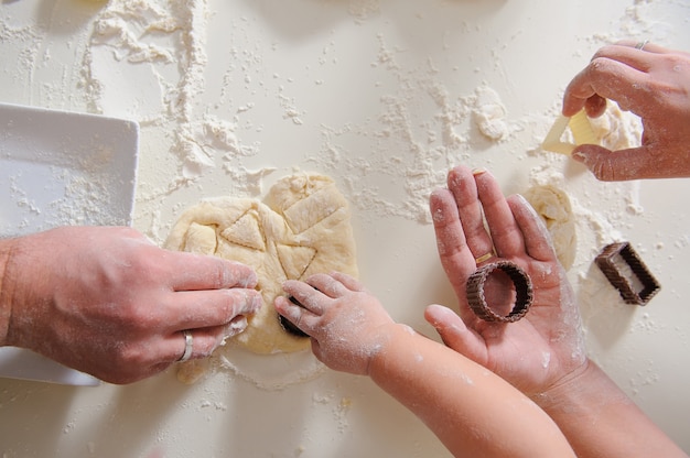 Tres pares de manos hacen galletas caseras, solo manos. Cortadores de galletas para hornear galletas con masa y harina