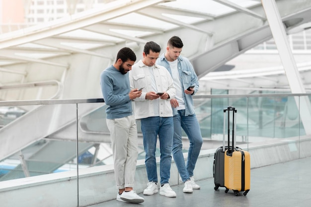 Tres pasajeros que usan las redes sociales en los teléfonos inteligentes en el aeropuerto