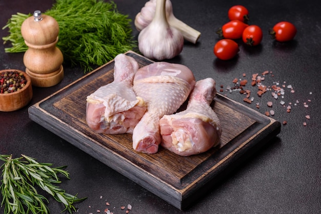 Tres patas de pollo crudo con especias y hierbas sobre una tabla para cortar madera