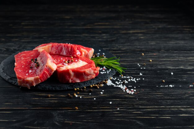 Três pedaços de carne crua suculenta em uma tábua de pedra em uma mesa de madeira preta.