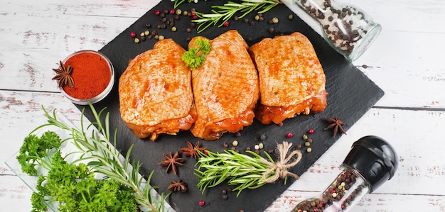 Três pedaços de coxas de frango marinadas em molho vermelho em uma tábua de cozinha