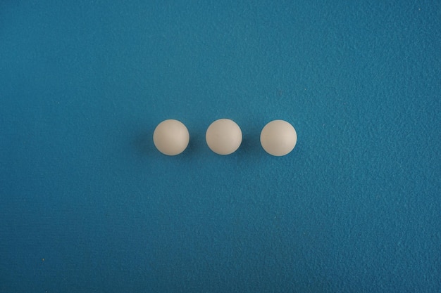 Tres pelotas de tenis de mesa se encuentran en fila sobre un fondo azul con una vista más cercana desde arriba Juego para el ocio Equipo deportivo Competición internacional Tenis de mesa Estilo de vida saludable