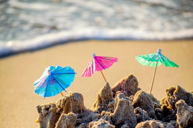 Tres pequeñas sombrillas de playa de papel para puesto de cócteles en arena