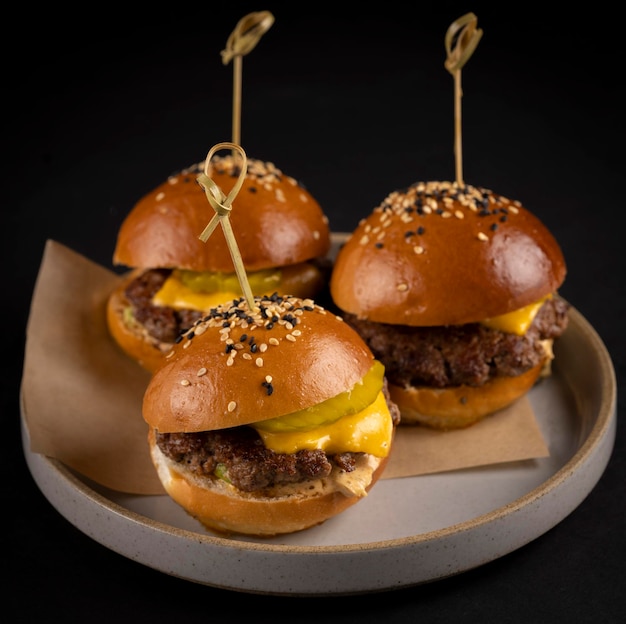 Foto três pequenos sanduíches de hambúrguer suculentos e bonitos em um fundo preto